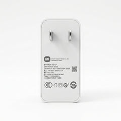A white Xiaomi power adapter with a white plug, shown from the back on a clean white background. The back features black printed specifications, a QR code, and various certification logos.