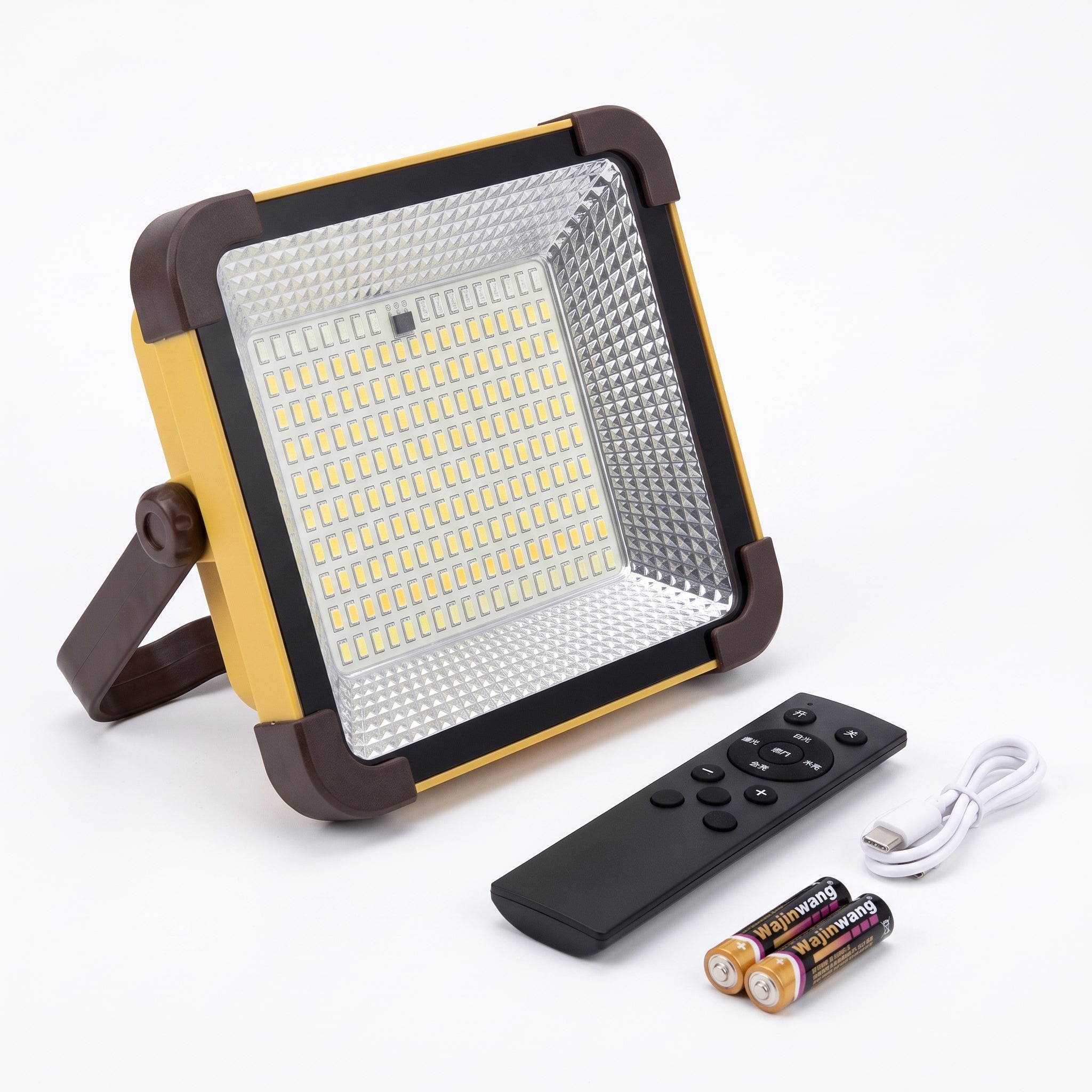 A square LED floodlight with a yellow and dark brown frame, shown with a black remote control, a white USB charging cable, and two batteries on a white background.