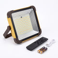 A square LED floodlight with a yellow and dark brown frame, shown with a black remote control, a white USB charging cable, and two batteries on a white background.
