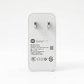 A white Xiaomi power adapter with a white plug, shown from the back on a clean white background. The back features black printed specifications, a QR code, and various certification logos.